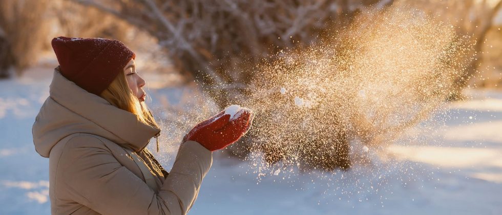 woman in winter blowing snow out of her hands