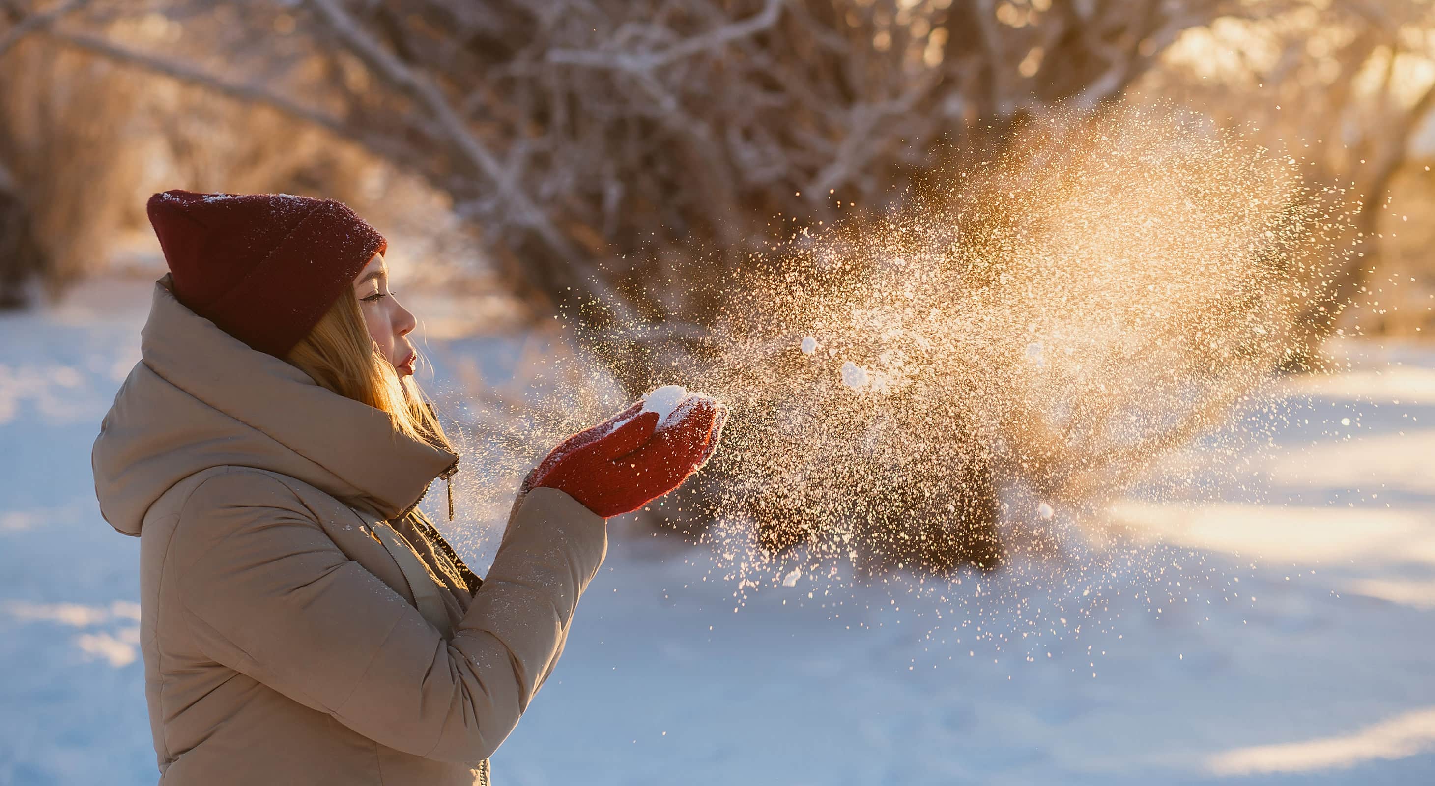 woman in winter blowing snow out of her hands