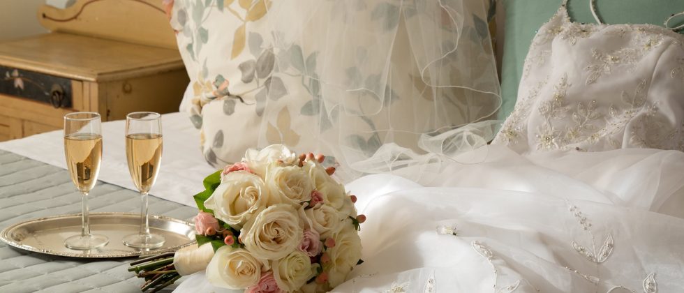 wedding dress, bouquet, and champagne on a bed
