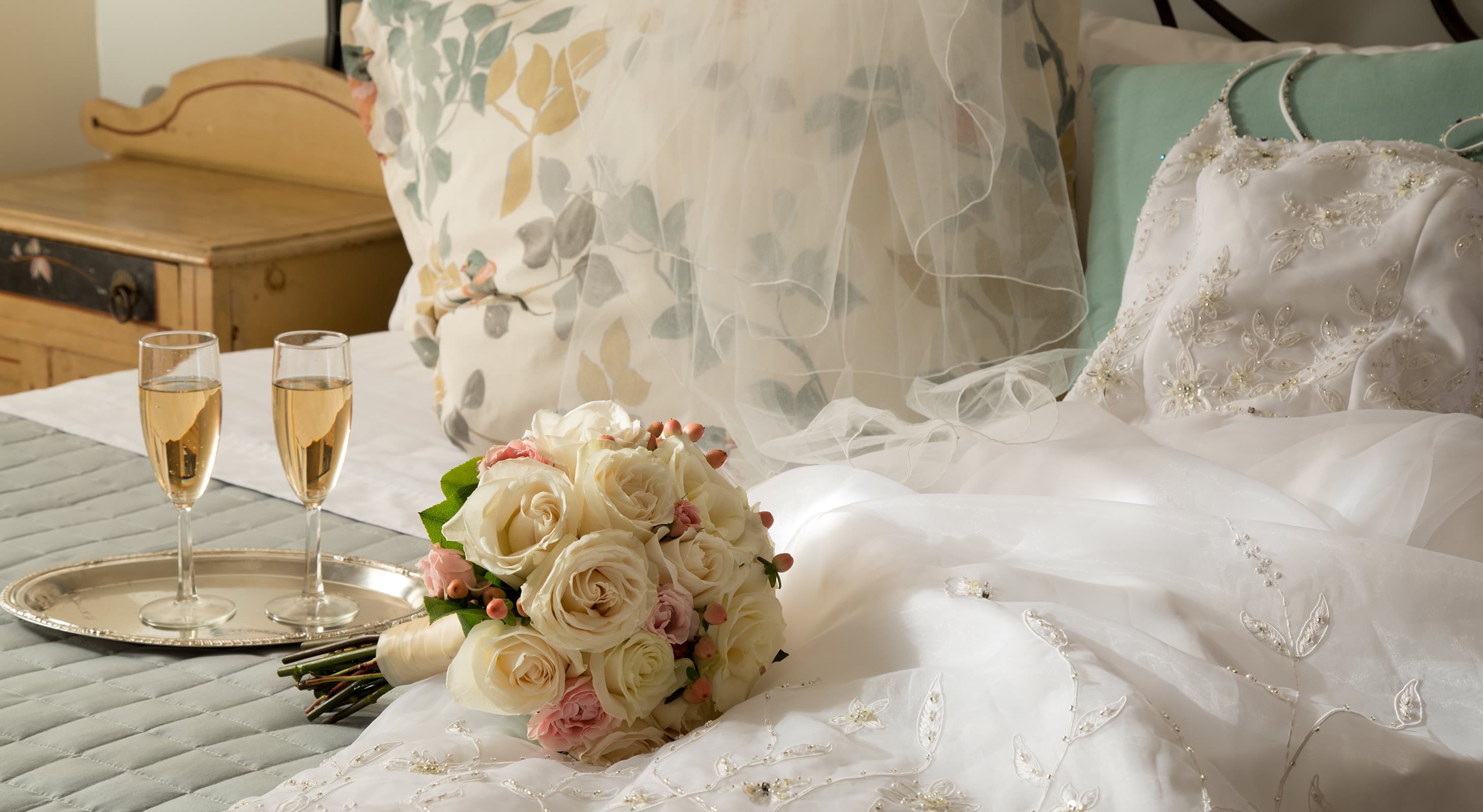 wedding dress, bouquet, and champagne on a bed