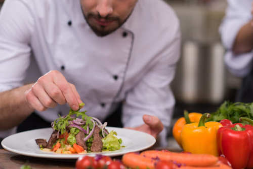 Close up of chef in a white coat adding herbs to a steak salad