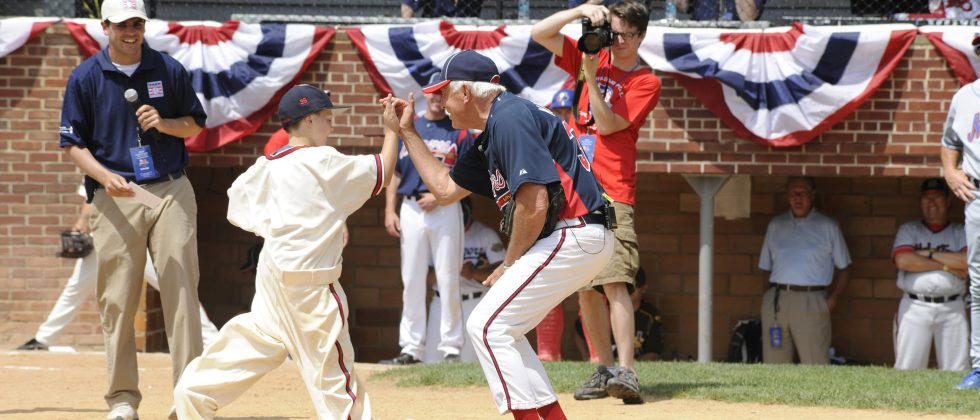 Man high-five a kid running to home plate on a baseball field