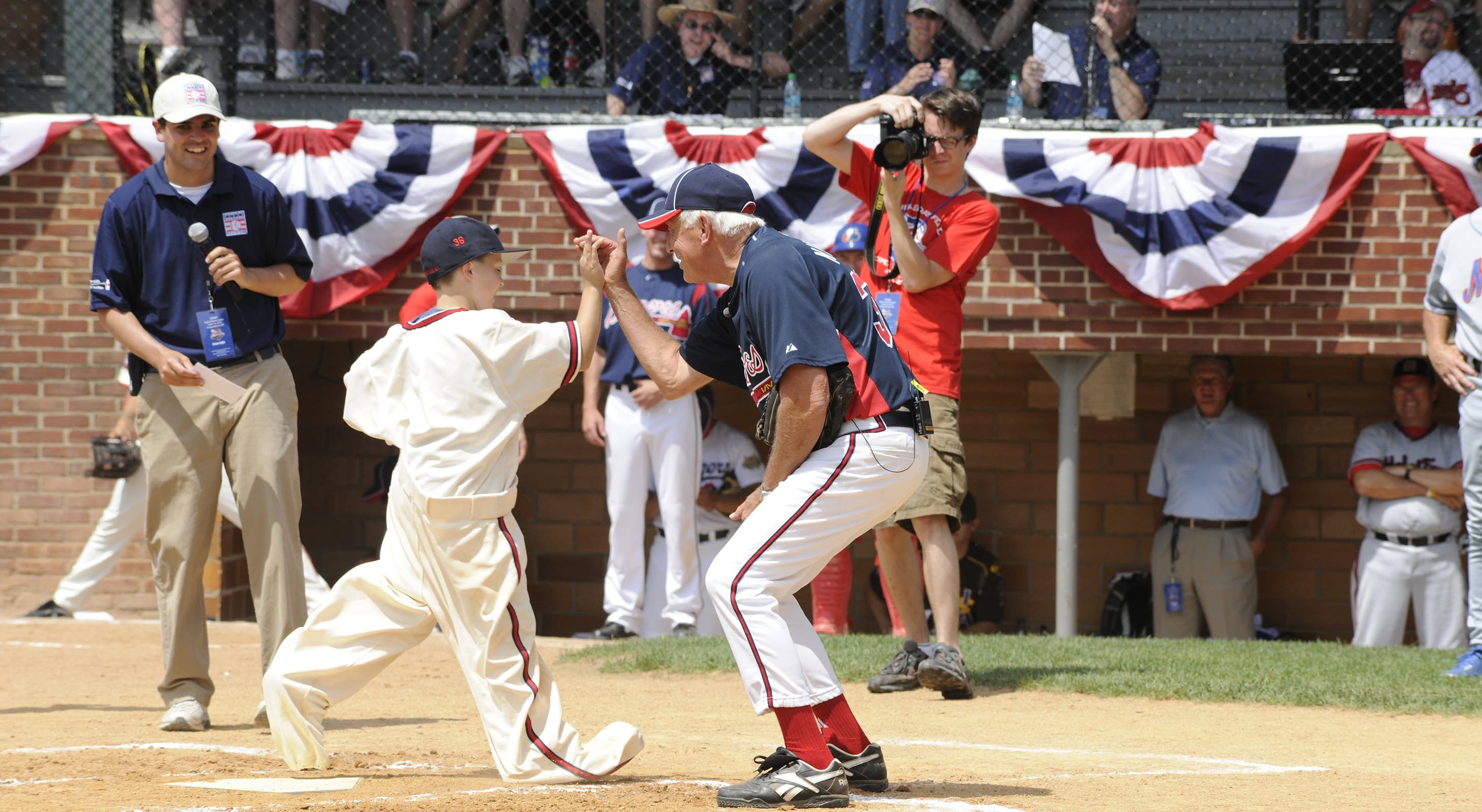 Man high-five a kid running to home plate on a baseball field in Cooperstown, NY